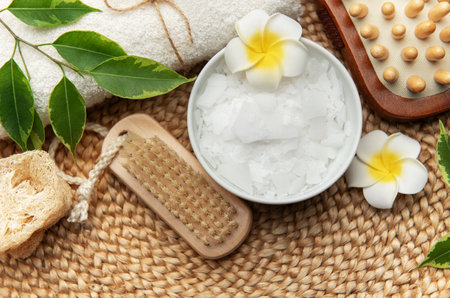 Wellness setting featuring magnesium chloride flakes, towel, loofah, brush and frangipani flowersの写真素材