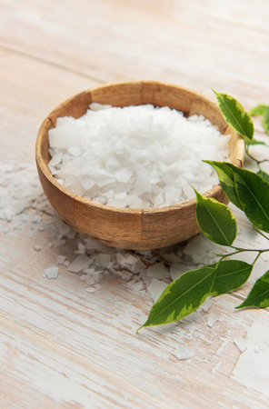 Magnesium chloride flakes in wooden bowl on rustic table with green leaves, promoting wellness and relaxationの写真素材