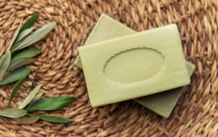 Natural olive oil soap bars are placed on a woven mat, accompanied by a fresh olive branch, promoting natural body care and hygieneの写真素材