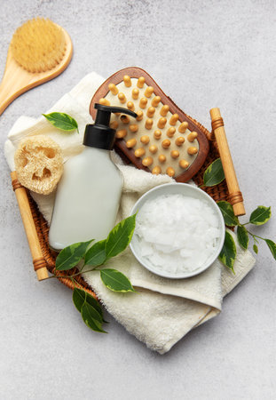 Natural bath salts, wooden massage brush, loofah sponge, and moisturizing lotion arranged on a wicker tray with fresh green leaves, promoting a spa like atmosphereの写真素材