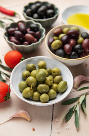 Variety of olives presented in bowls, accompanied by fresh ingredients like tomatoes, garlic, olive oil, salt, and pepper flakes, creating an inviting culinary sceneの写真素材