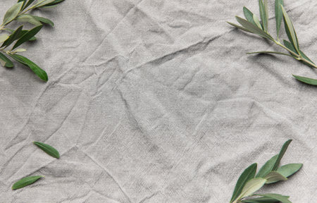 Olive branches creating a border on a gray linen cloth background, offering a textured and natural backdropの写真素材