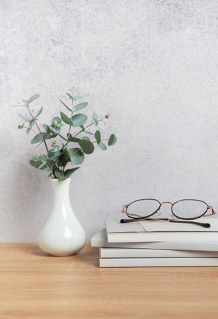 Eyeglasses sit atop a stack of books beside a vase of eucalyptus branches, embodying a peaceful reading atmosphereの写真素材