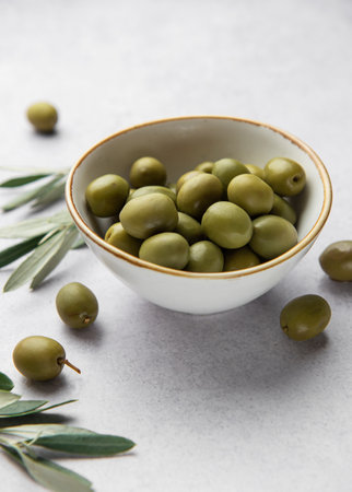 Fresh green olives are served in a white bowl, accompanied by olive branches, creating a mediterranean culinary sceneの写真素材