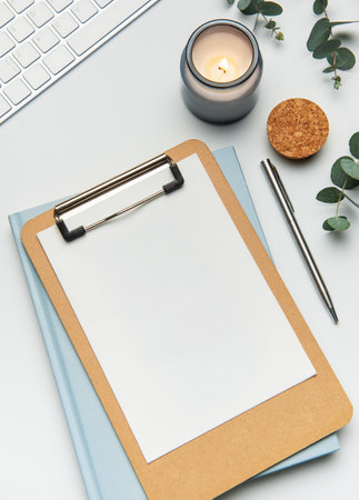 Clipboard, keyboard, pen, candle and eucalyptus leaves creating a relaxing workspace on white tableの写真素材