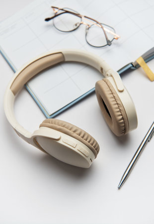 Modern wireless headphones, planner, eyeglasses and pen are lying on white table, representing concept of remote work or studyingの写真素材