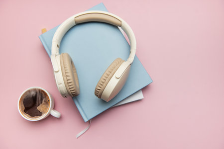 Modern wireless headphones sit atop a stack of books alongside a cup of coffee, creating a cozy and productive atmosphereの写真素材