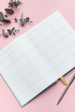 Open notebook with blank pages, pen, and eucalyptus leaves on a pink background, inviting planning and organizationの写真素材