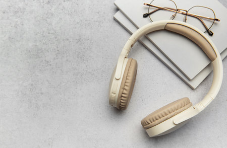 Beige wireless headphones, books, and eyeglasses arranged on a gray textured surface, creating a cozy and productive atmosphereの写真素材