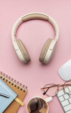 Home office desk workspace with wireless headphones, coffee, keyboard, eyeglasses, and notebook on a pink background, representing work from home or telecommutingの写真素材
