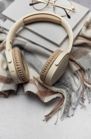 Beige wireless headphones, eyeglasses, book, and warm plaid on gray background create cozy autumn atmosphereの写真素材