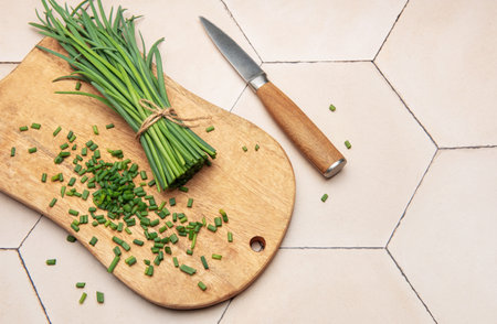 Fresh chives bunch and chopped chives on wooden cutting board with knife on kitchen tableの写真素材