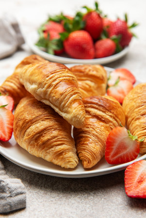 Golden brown croissants are beautifully arranged on a white plate with fresh strawberries, creating a tempting breakfast sceneの写真素材