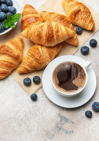 Freshly baked croissants, blueberries and steaming cup of coffee composing a tasty breakfastの写真素材