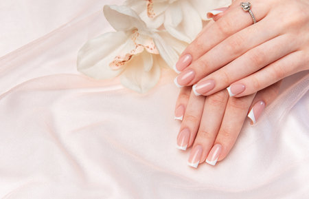 Woman's hands with perfect french manicure on pink silk fabric with orchid flowerの写真素材