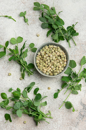 Dried split peas in bowl surrounded by fresh pea shoots, creating a healthy and vibrant culinary...