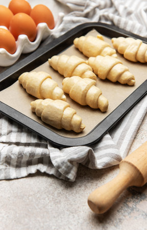 Raw croissants on a baking sheet with eggs and rolling pin, ready to be bakedの写真素材