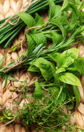 Freshly harvested herbs, including chives, mint, rosemary, basil, and thyme, are neatly bundled and arranged on a rustic woven tray, ready to enhance culinary creationsの写真素材