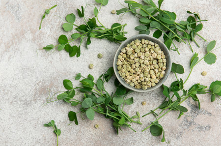 Dried split peas in bowl surrounded by fresh pea shoots, creating a healthy and vibrant culinary...