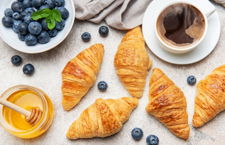 Freshly baked croissants are served for breakfast with blueberries, honey and a cup of black coffeeの写真素材
