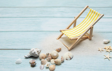 Miniature deck chair sits on a sandy beach surrounded by seashells, evoking a sense of summer vacation and relaxationの写真素材