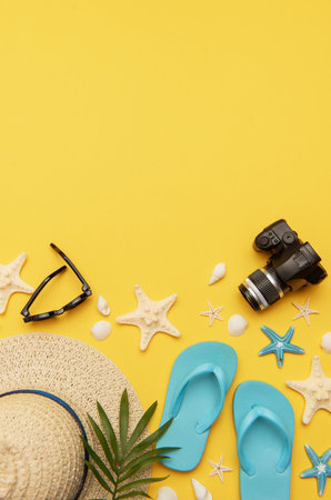 Beach accessories like flip flops, sunglasses, straw hat, seashells, starfish and camera composing a summer travel flat lay on a vibrant yellow background with empty space for text or advertisingの写真素材