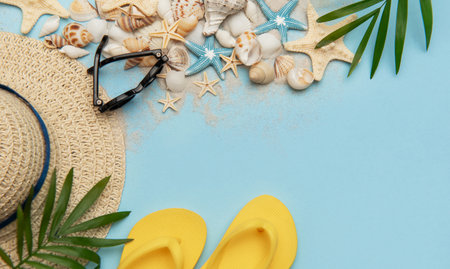 Summer holiday beach background with seashells, sunglasses, flip flops, and straw hat on blue backgroundの写真素材