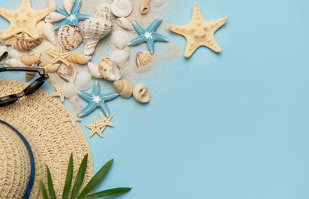 Beach accessories including seashells, sunglasses, straw hat and sand on blue background forming...