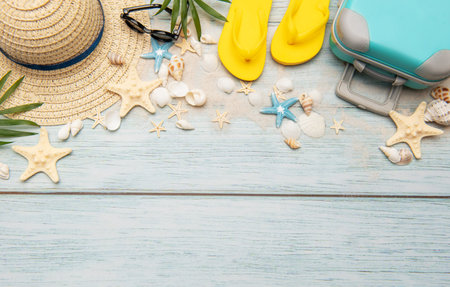 Suitcase, sunglasses, straw hat, starfish, seashells and flip flops composing a summer frame on light blue wooden background with copy spaceの写真素材