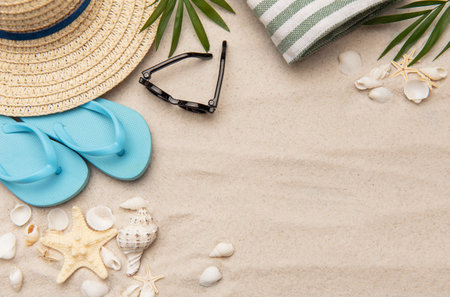 Summer accessories such as flip flops, sunglasses and a straw hat are lying on white sand with seashells and starfishの写真素材