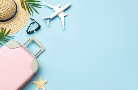 Travel accessories concept with pink suitcase, airplane model, sunglasses and straw hat on blue background with copy spaceの写真素材