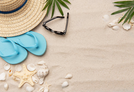 Summer accessories such as flip flops, sunglasses and a straw hat are lying on white sand with seashells and starfishの写真素材