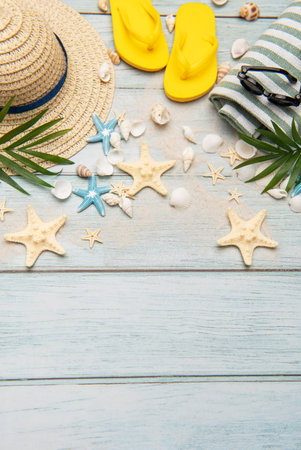 Beach accessories like flip flops, sunglasses, straw hat, seashells and starfishes arranged on wooden background with sand creating a frame with copy spaceの写真素材