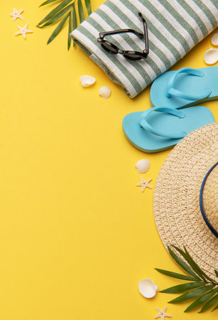Beach accessories like flip flops, sunglasses, straw hat and towel on yellow background with copy spaceの写真素材