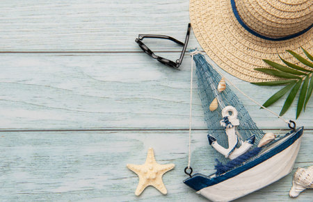 Summer composition with straw hat, sunglasses, seashells, starfish and decorative sailboat on light blue wooden planks evoking beach holidaysの写真素材