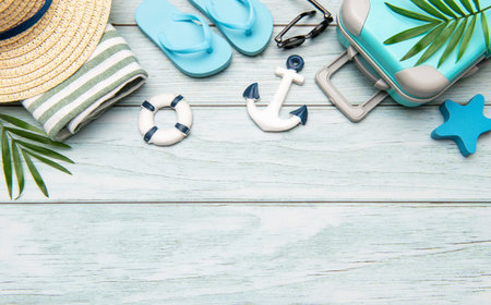 Beach accessories like flip flops, sunglasses, a straw hat, a towel, an anchor, a lifebuoy and a suitcase lying on a wooden backgroundの写真素材