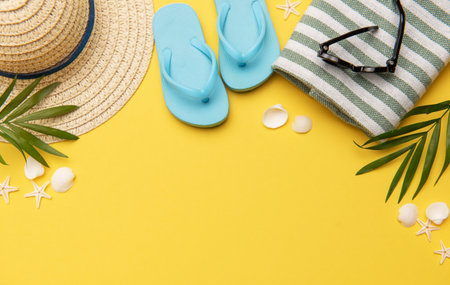Beach accessories like flip flops, sunglasses, straw hat and towel on yellow background with copy spaceの写真素材