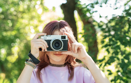 Woman photographing outdoors with retro camera in a lush green settingの写真素材