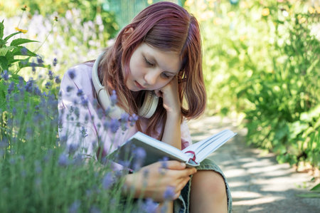 Teen student enjoying reading a book in a peaceful garden setting, surrounded by lavender flowersの写真素材