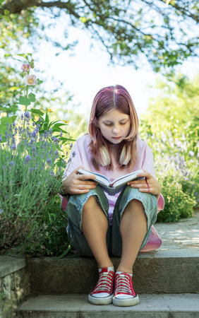 Girl sitting on steps in a garden, engrossed in reading a bookの写真素材