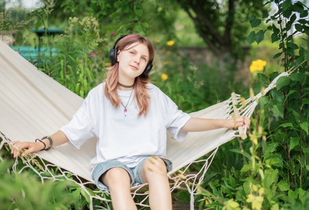 Teenager relaxing in hammock and listening to music with headphones in a garden