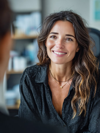 Businesswoman listening attentively and smiling during a productive meeting with a colleague in a modern officeの素材