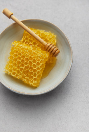 Golden honeycomb and wooden honey dipper sit in a ceramic bowl, ready for a sweet treat