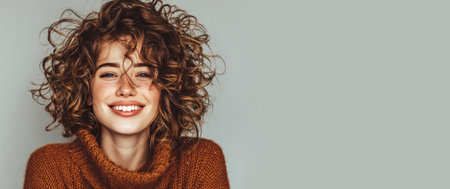 Studio portrait of cheerful young woman with curly ginger hair and freckles wearing a turtleneck sweater, smiling and showing teethの素材