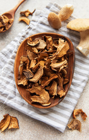 Dried porcini mushrooms on a wooden plate, fresh porcini mushrooms and a kitchen towel create a cozy autumnal sceneの写真素材