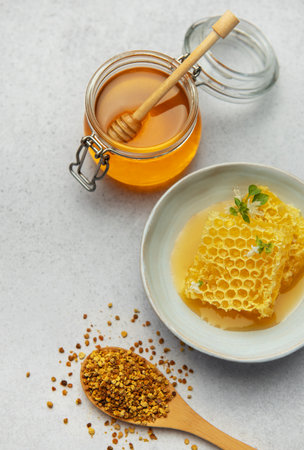 Golden honey, honeycomb and bee pollen are creating a delicious and healthy composition on a light...