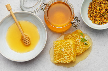Golden honey, honeycomb, and pollen arranged on a textured surface, highlighting natural sweeteners...