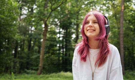 Teenager with pink hair enjoying music in nature, sitting on a tree trunk