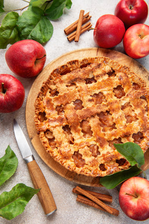 Homemade apple pie surrounded by fresh red apples, cinnamon sticks and apple leaves, creating a warm and inviting autumnal sceneの写真素材