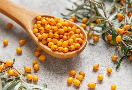 Ripe sea buckthorn berries spilling from wooden spoon onto textured surface, showcasing vibrant...